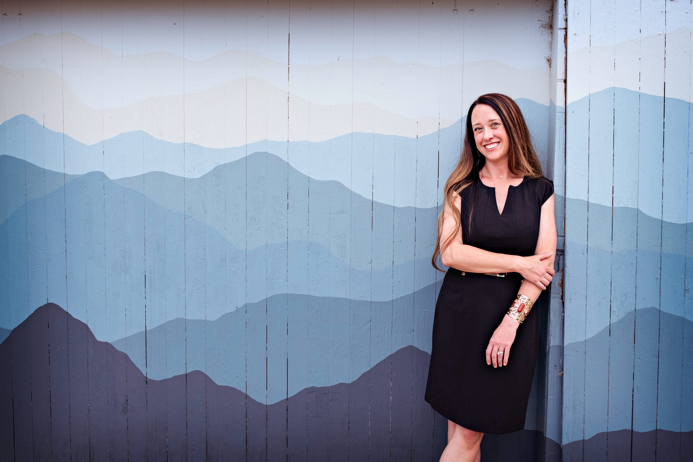 Stephanie Drobny standing against a blue-gray painted mountain mural, smiling toward the camera